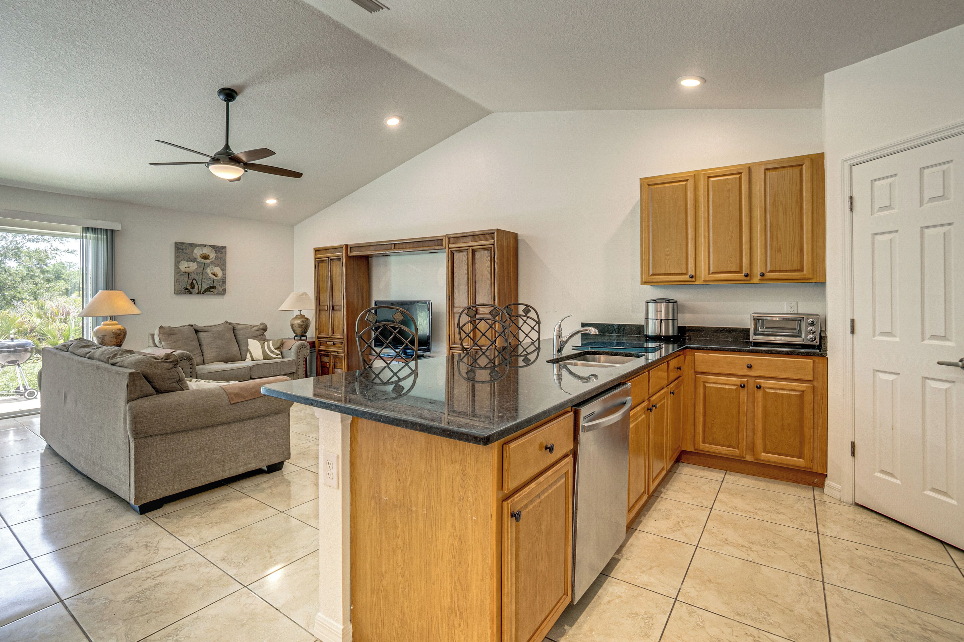 A kitchen with wooden cabinets, a central island, a dining area with a sofa, and a ceiling fan.