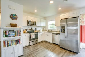 A kitchen with white cabinets, a stainless steel refrigerator, a microwave, a stove, and a bookshelf with books. - Serene Punta Gorda Home Near the Peace River (Punta Gorda)