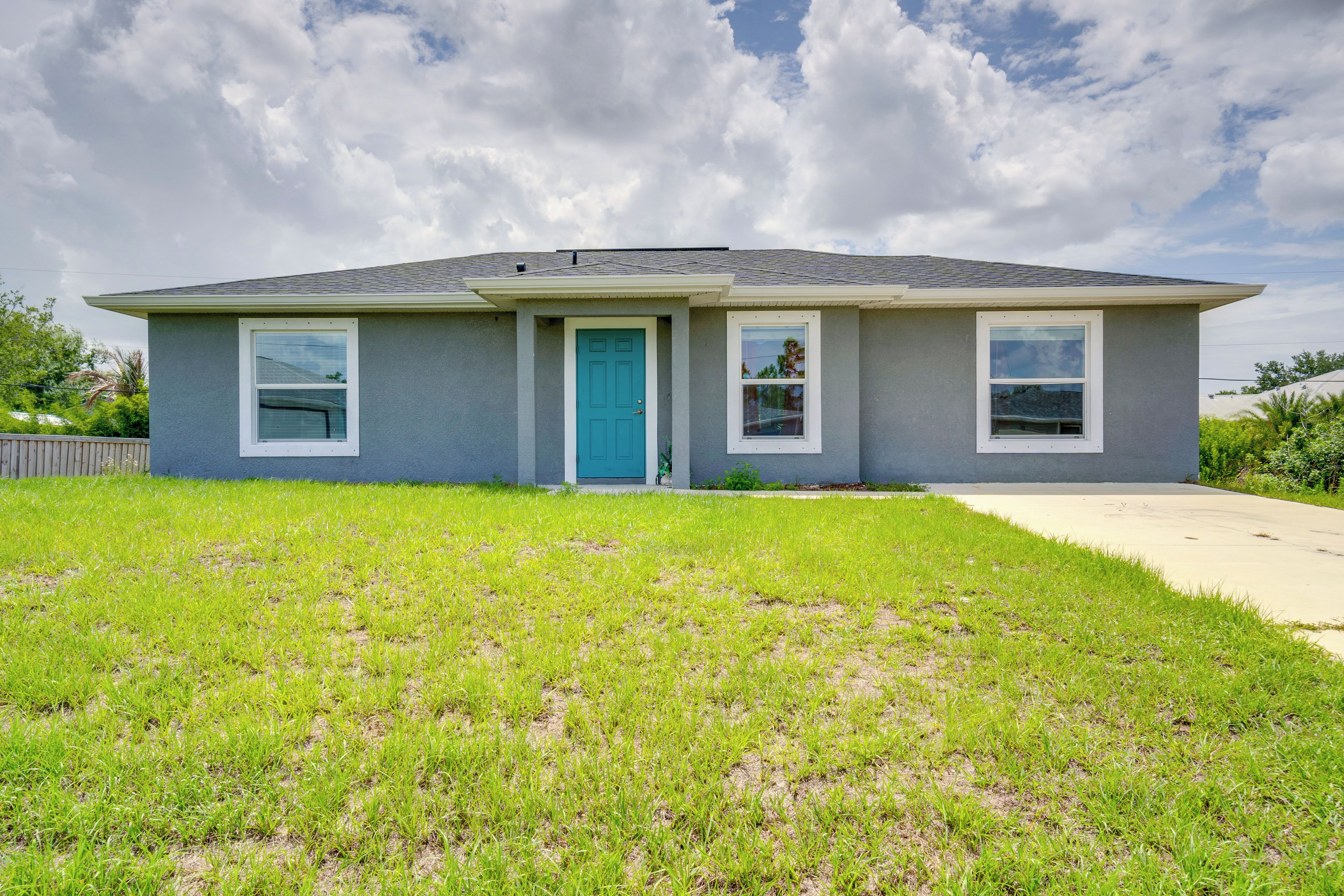 A single-story house with a blue door, two windows on the front, and a grassy lawn.