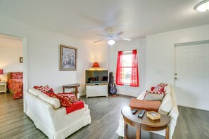 A living room with a white sofa, a red and white patterned sofa, a wooden coffee table, a television, a guitar, and a red curtain. - Serene Punta Gorda Home Near the Peace River (Punta Gorda)