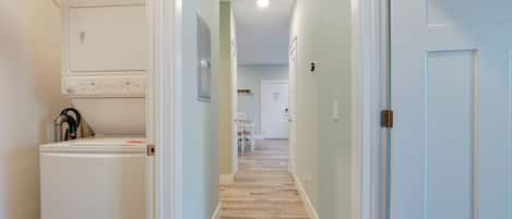 Un couloir étroit, avec un coin buanderie sur la gauche, une porte au fond et un interrupteur sur le mur.