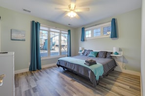 Un dormitorio con cama, ventilador de techo, ventana y mesita de noche.