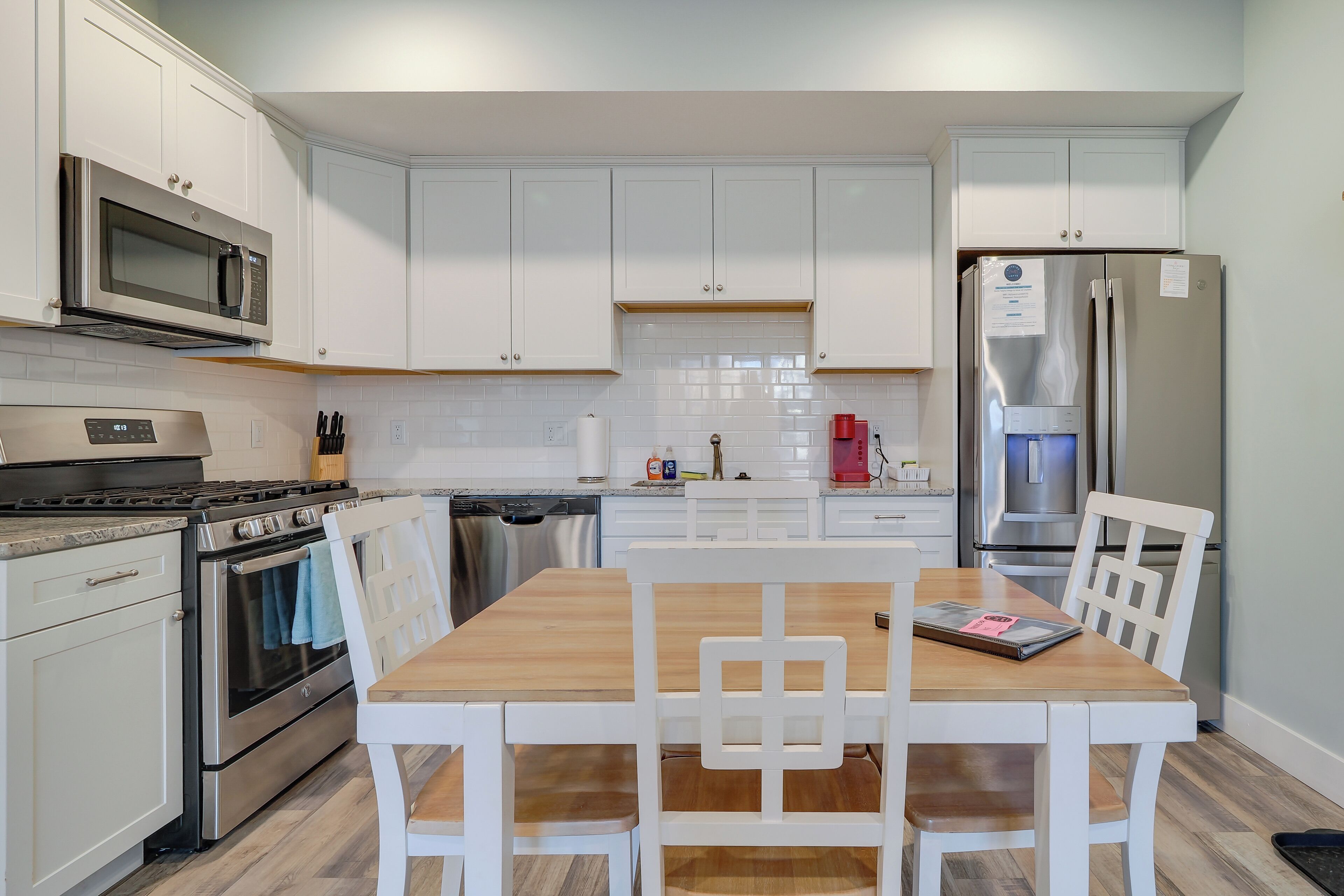 A modern kitchen with white cabinets, stainless steel appliances, and a wooden dining table with white chairs.