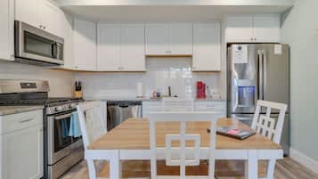 A modern kitchen with white cabinets, stainless steel appliances, and a wooden dining table with white chairs.