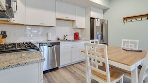 A modern kitchen with white cabinets, stainless steel appliances, and a wooden dining table with white chairs.