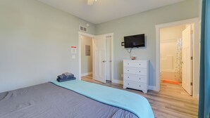 A bedroom with a bed, a dresser, a television, and a door leading to a bathroom.