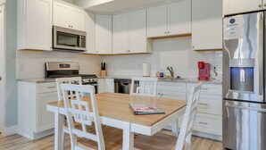 Una cocina moderna con armarios blancos, electrodomésticos de acero inoxidable y una mesa de comedor de madera.
