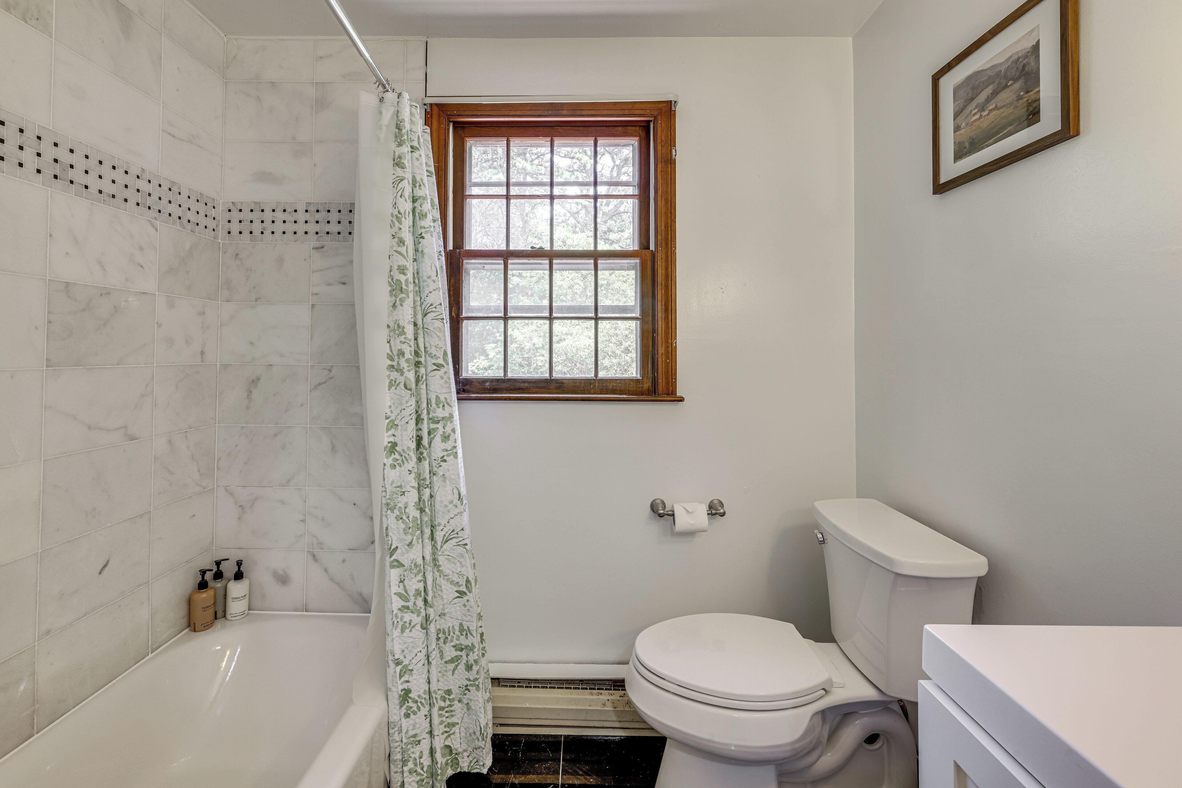 A bathroom with a bathtub, toilet, and a window.