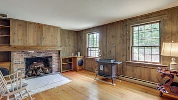 Une pièce aux murs en bois, avec une cheminée, une grande fenêtre et un poêle à bois.