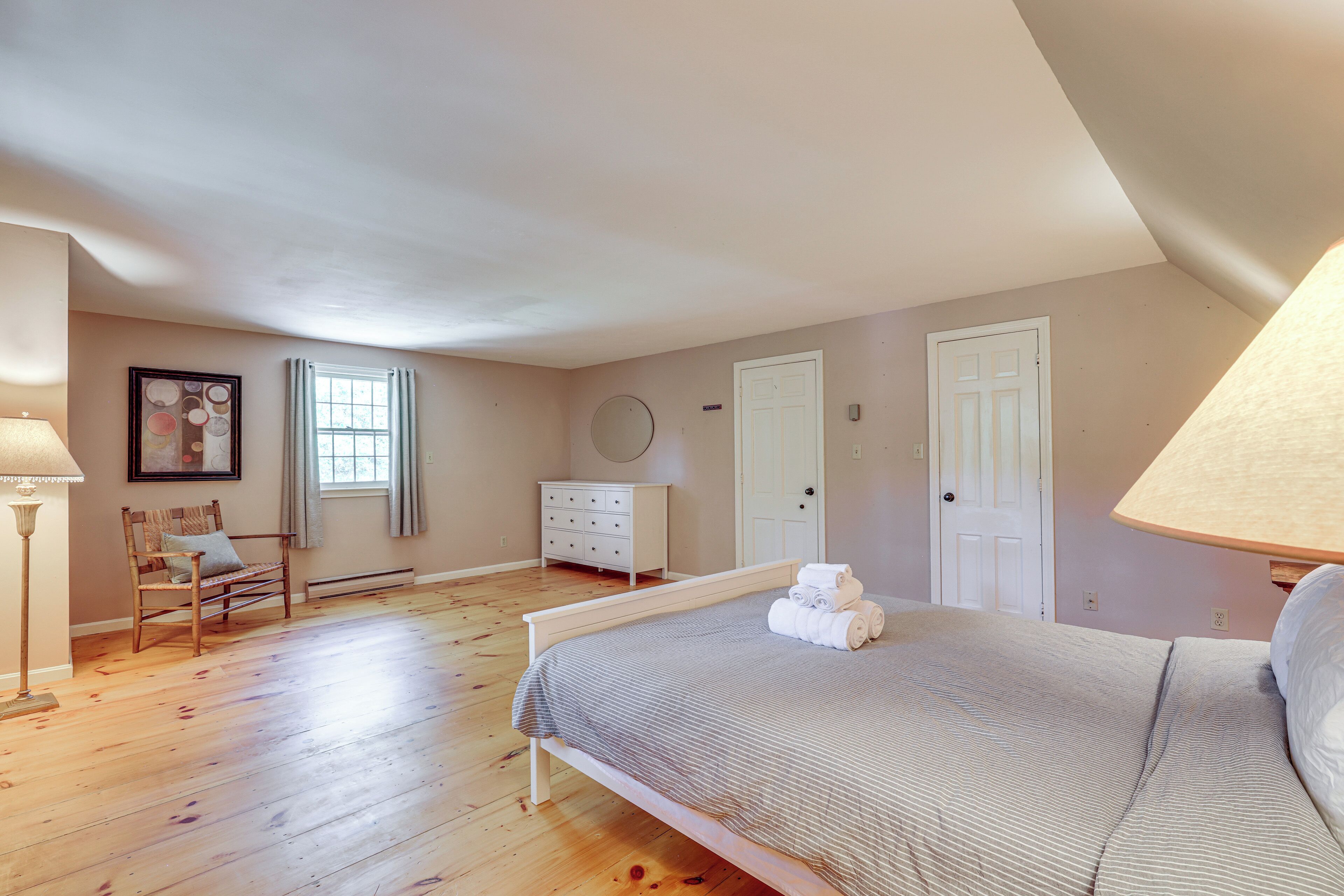 Um quarto com uma cama, cômoda, cadeira, janela e abajur.