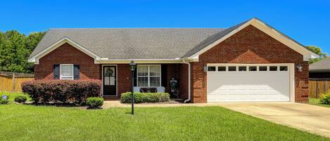 A single-story brick house with a front garage, a small front porch, and a well-maintained lawn.