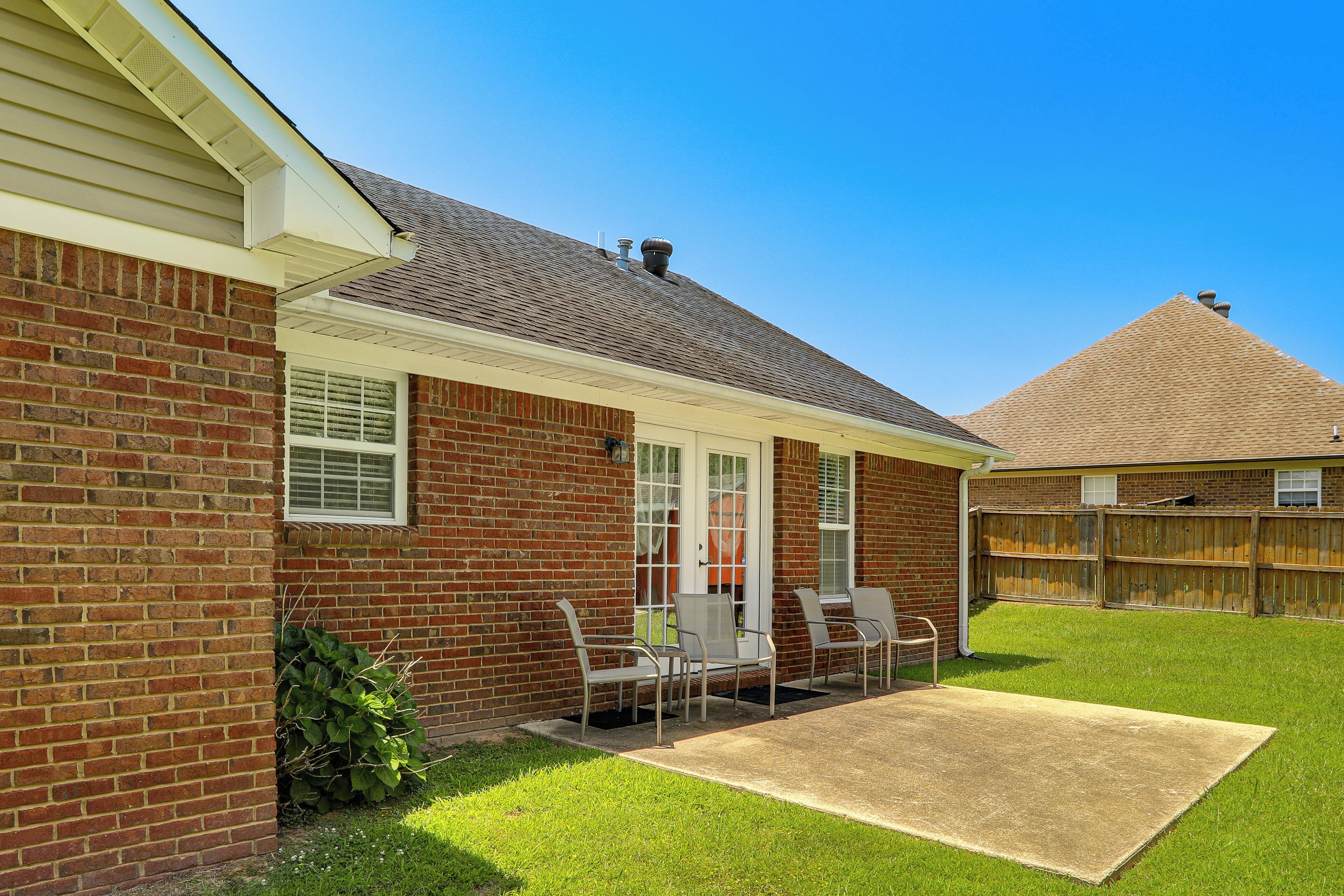 A brick house with a covered patio, a fenced backyard, and a clear sky.