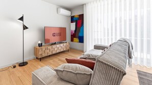 Un salon moderne avec un téléviseur à écran plat, un lampadaire, une console en bois, une peinture abstraite aux couleurs vives et un canapé gris.