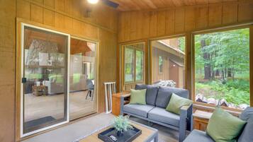 A modern interior with a wooden ceiling, large sliding glass doors, a grey sofa with green cushions, and a small table with a tray.