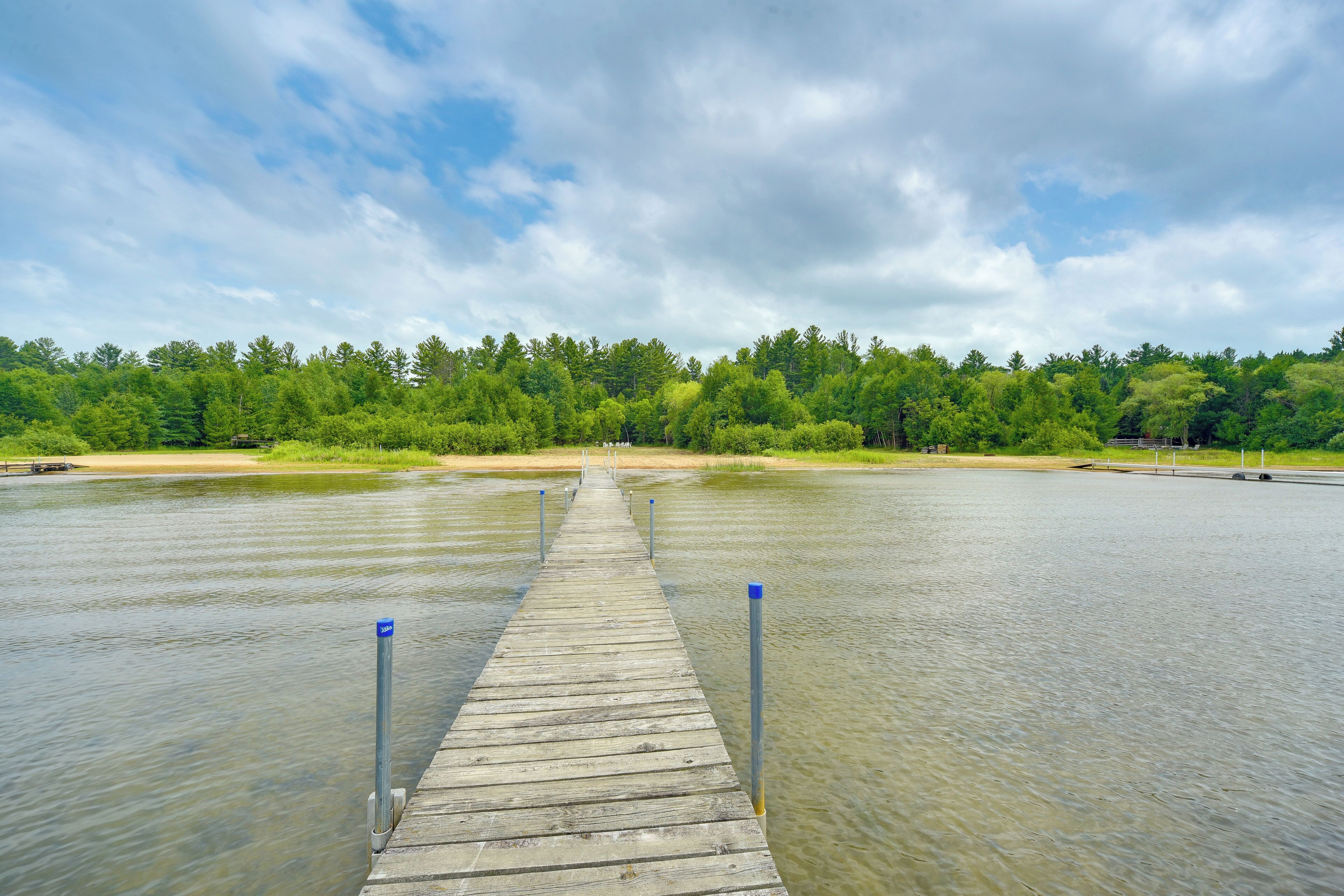 A wooden pier extending into a calm body of water, surrounded by dense green trees and a clear sky.