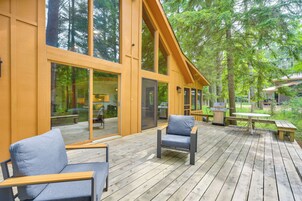 Una terraza de madera con mobiliario exterior, ventanas amplias y vistas del bosque circundante.