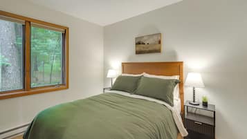 Ein Schlafzimmer mit großem Fenster, einem Bett mit grüner Bettwäsche, zwei Nachttischen mit Lampen und einem Gemälde an der Wand.
