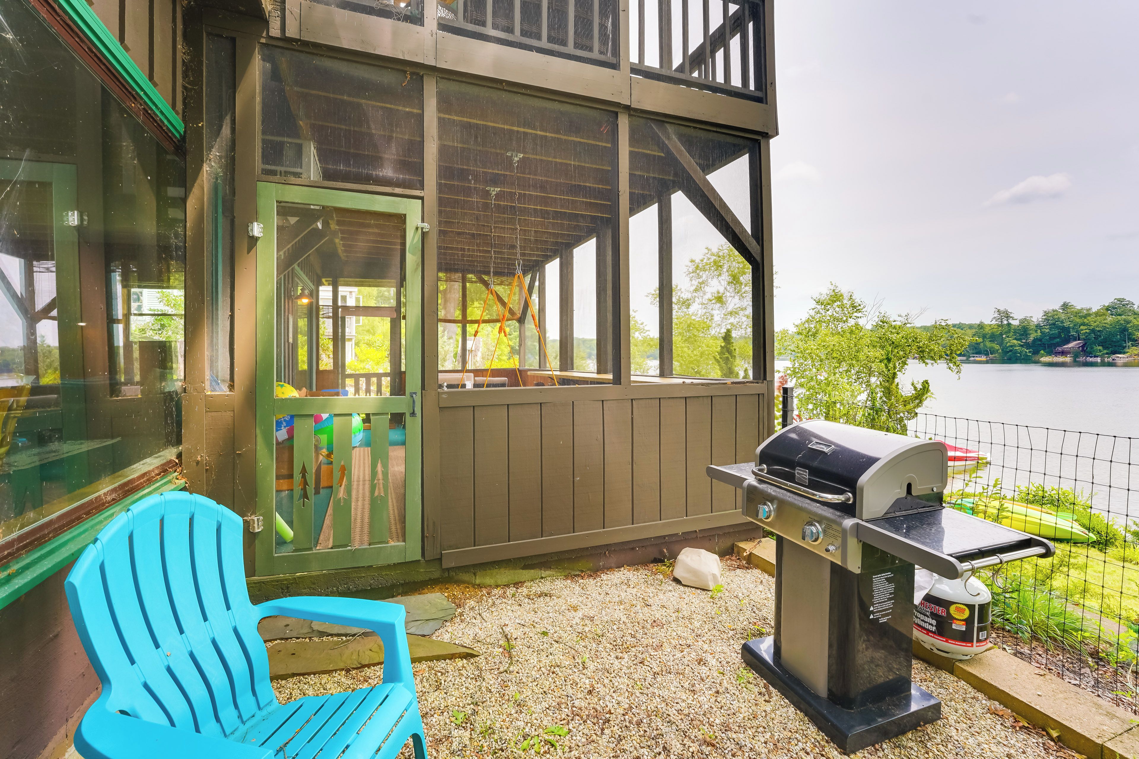 Un espace extérieur abrité, équipé d’un barbecue, d’une chaise bleue et offrant une vue sur un lac.