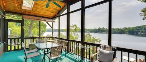 Terraza techada al aire libre con una mesa y sillas, con vista a un lago.