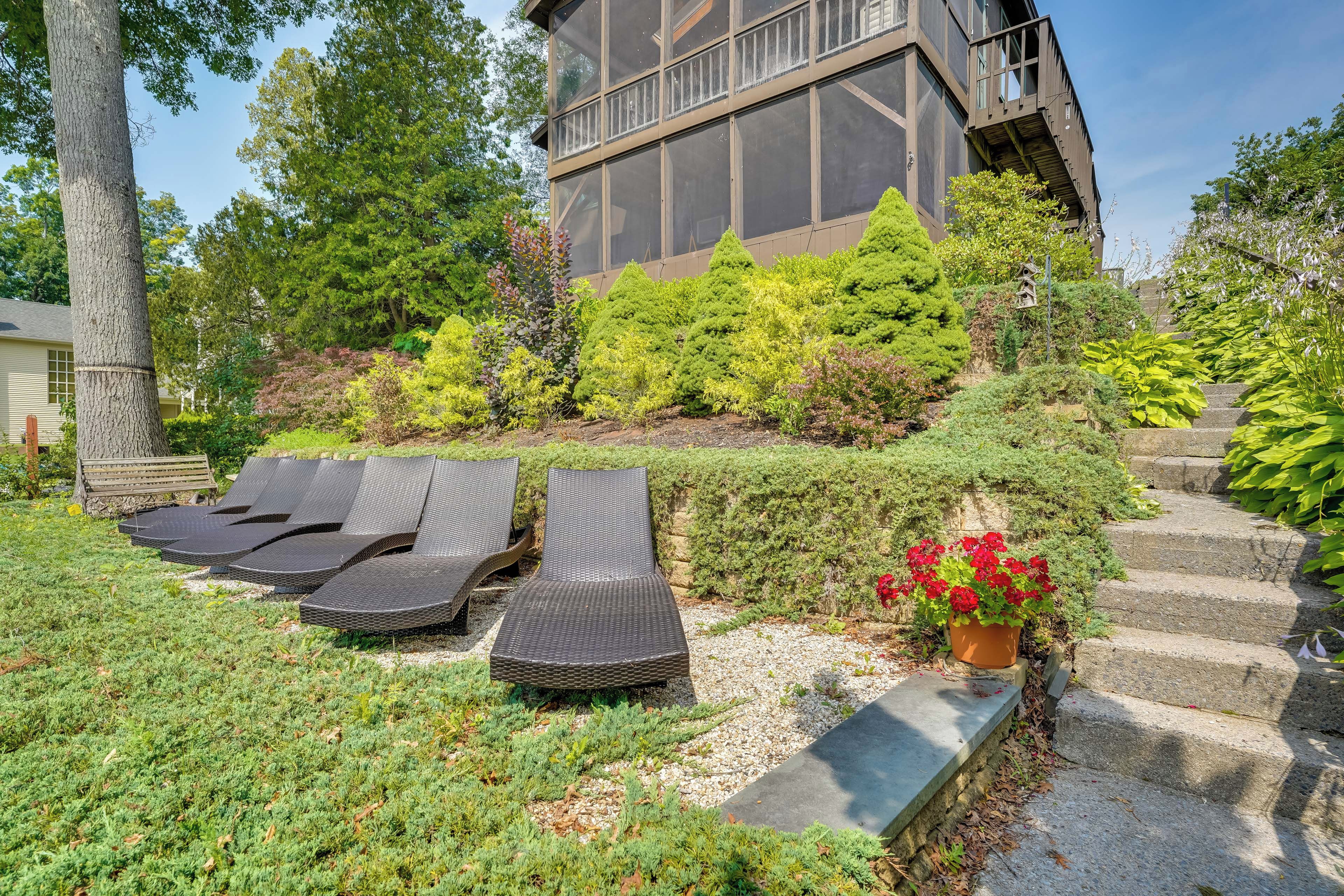 Un bâtiment moderne doté d’une grande façade en verre, d’un escalier en pierre et d’un jardin agrémenté de chaises longues et de plantes en pot.