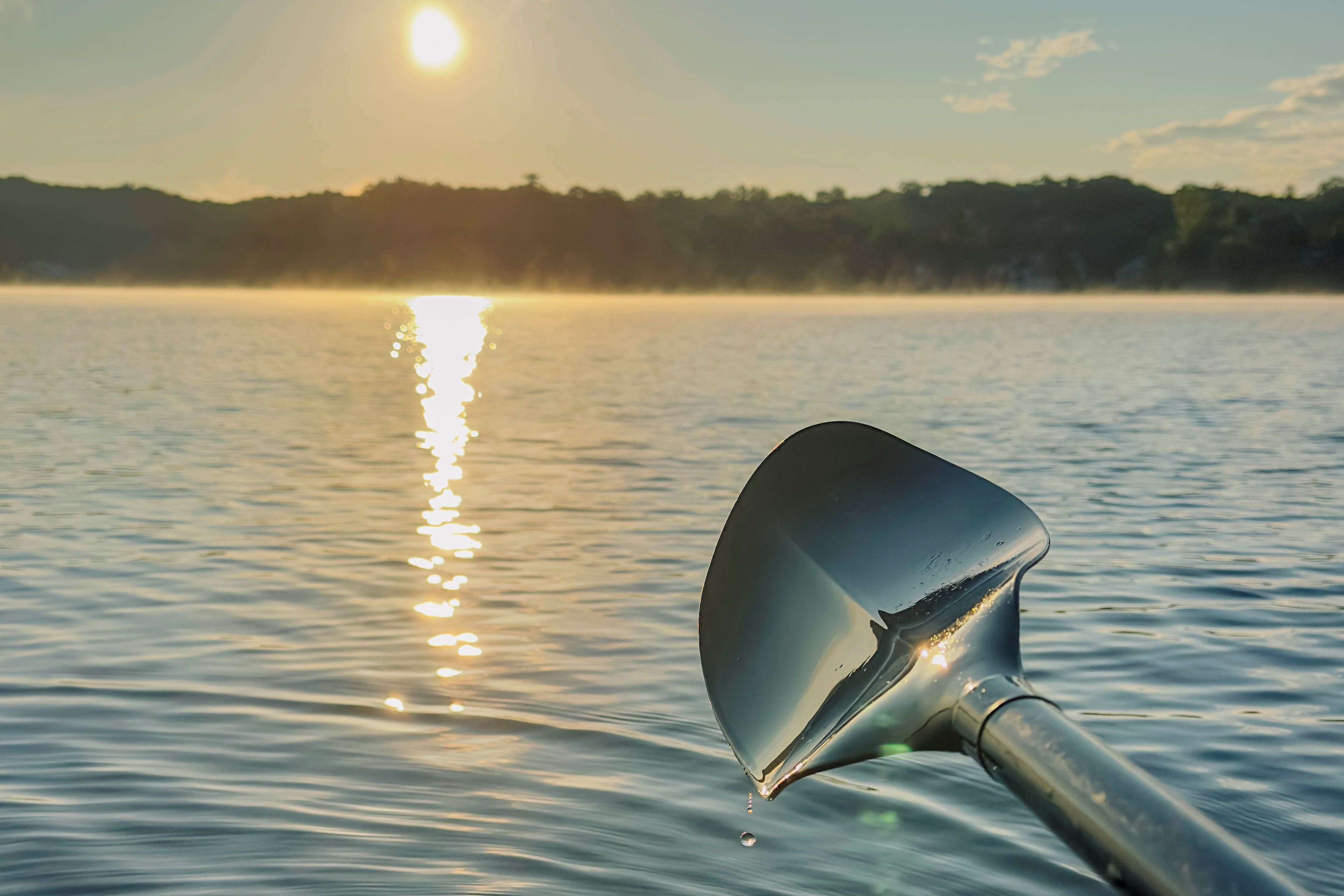 A boat's bow with a metal scoop in the water, reflecting the sun's rays.