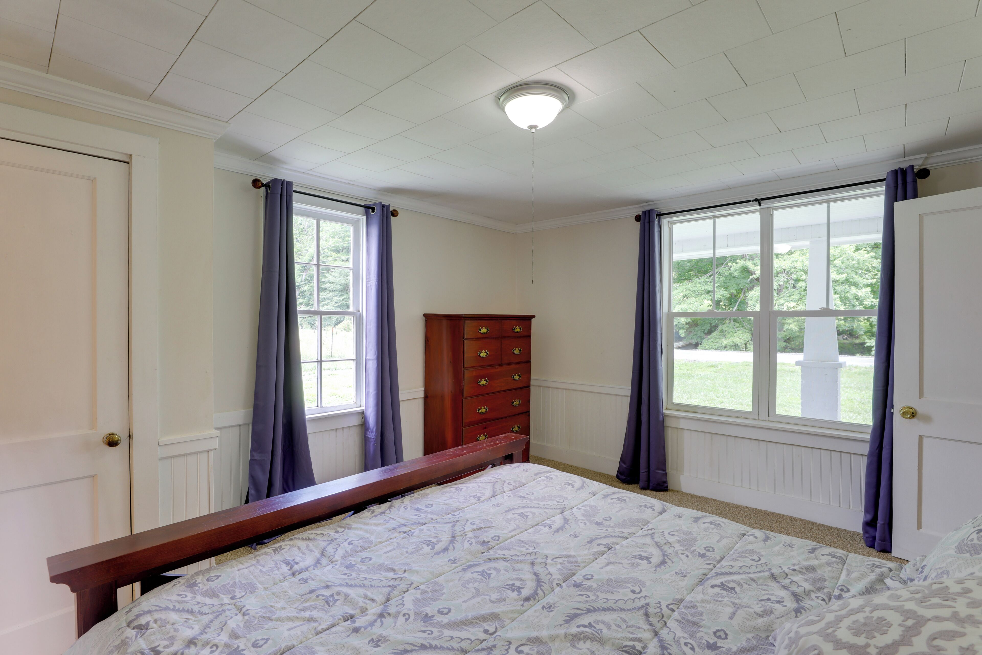 Un dormitorio con cama, cómoda y dos ventanas con cortinas.