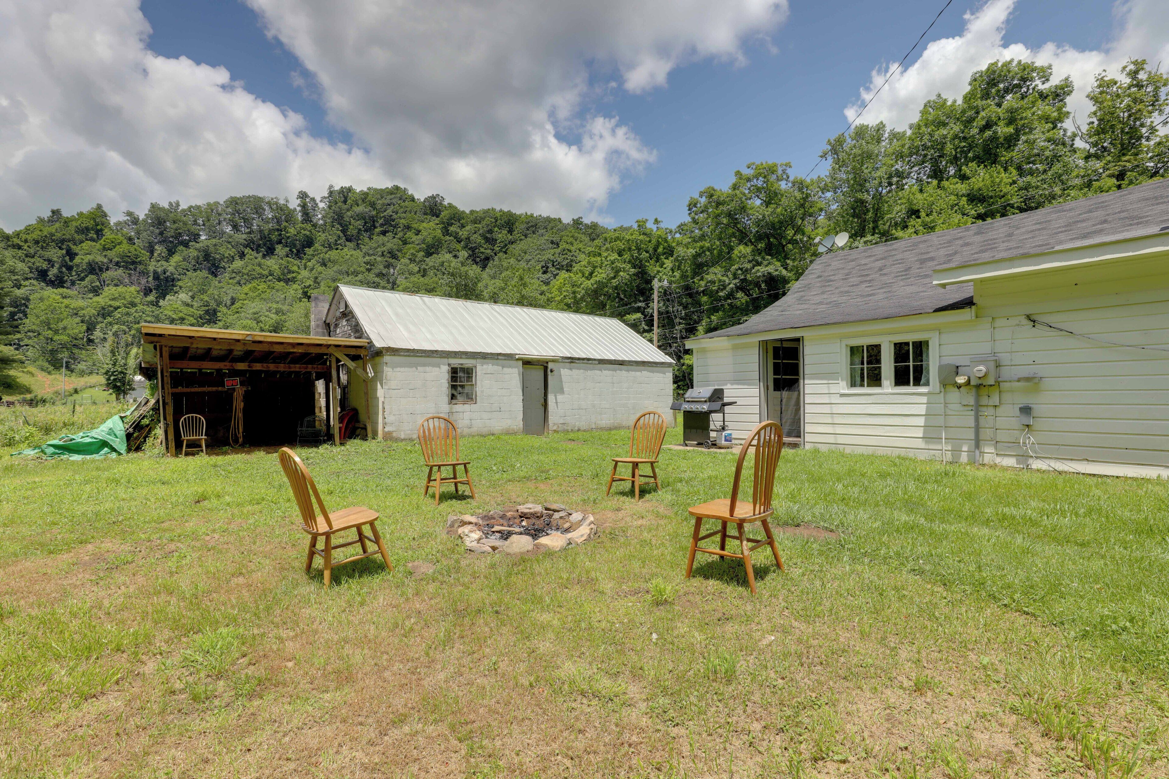 A grassy backyard with a fire pit, wooden chairs, a shed, and a house with a satellite dish.