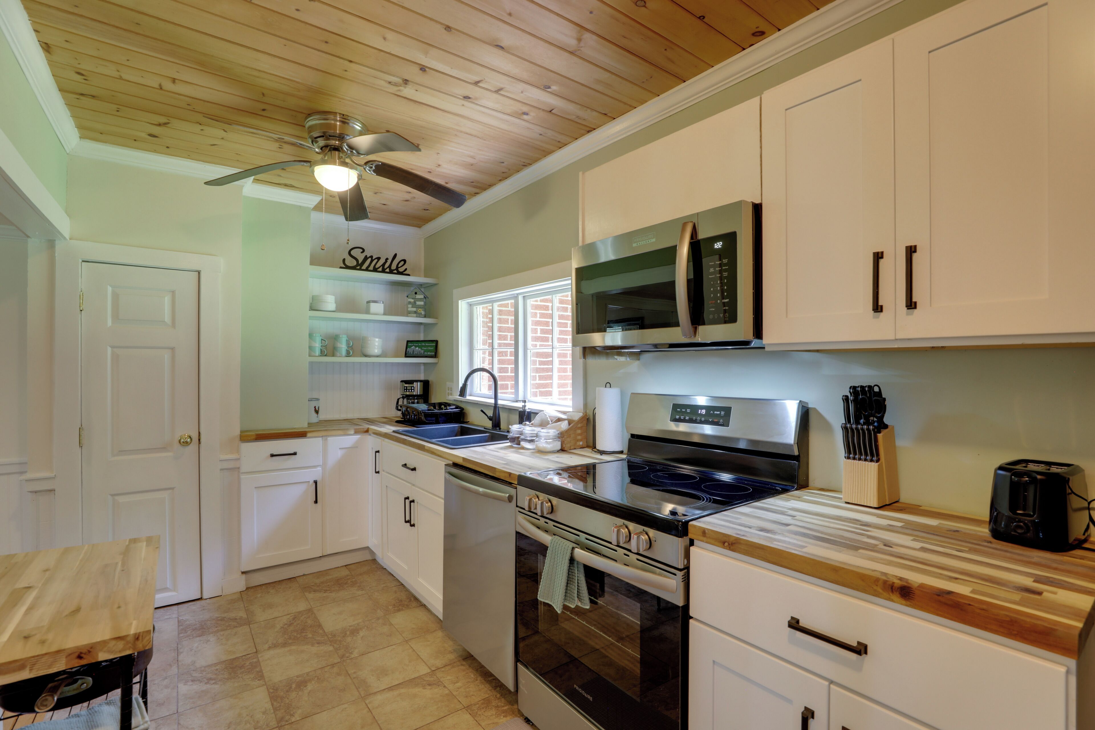 A kitchen with white cabinets, a microwave, stove, and a ceiling fan.