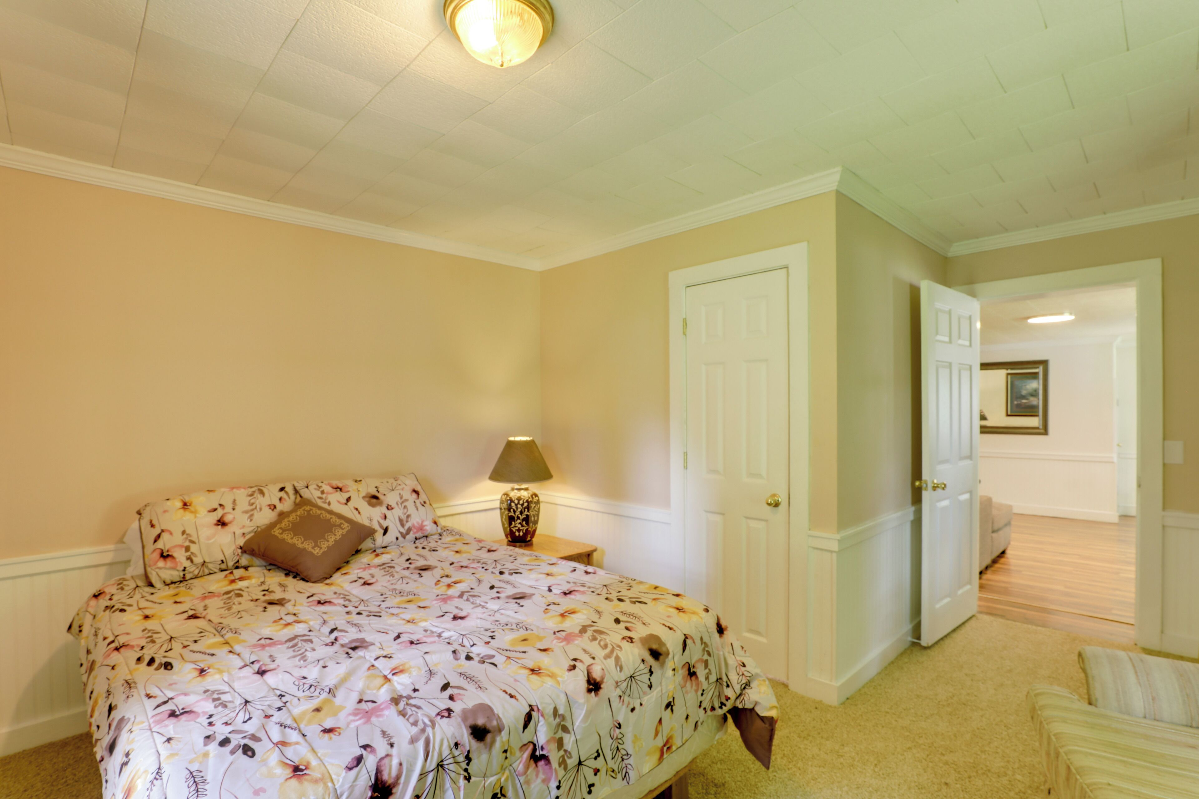 Une chambre à coucher avec une couvre-lit à motifs floraux, une lampe de chevet, une porte et un couloir menant à une autre pièce.