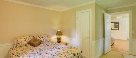 Une chambre à coucher avec une couvre-lit à motifs floraux, une lampe de chevet, une porte et un couloir menant à une autre pièce.