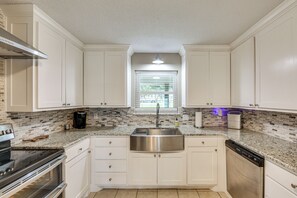 A kitchen with white cabinets, a stainless steel sink, a dishwasher, and a window with blinds. - Cedar Creek Lake 'amarianna Cove' Paradise! (Mabank)