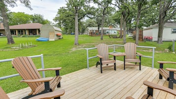 A deck with wooden chairs and tables, a small shed, and a house in the background.