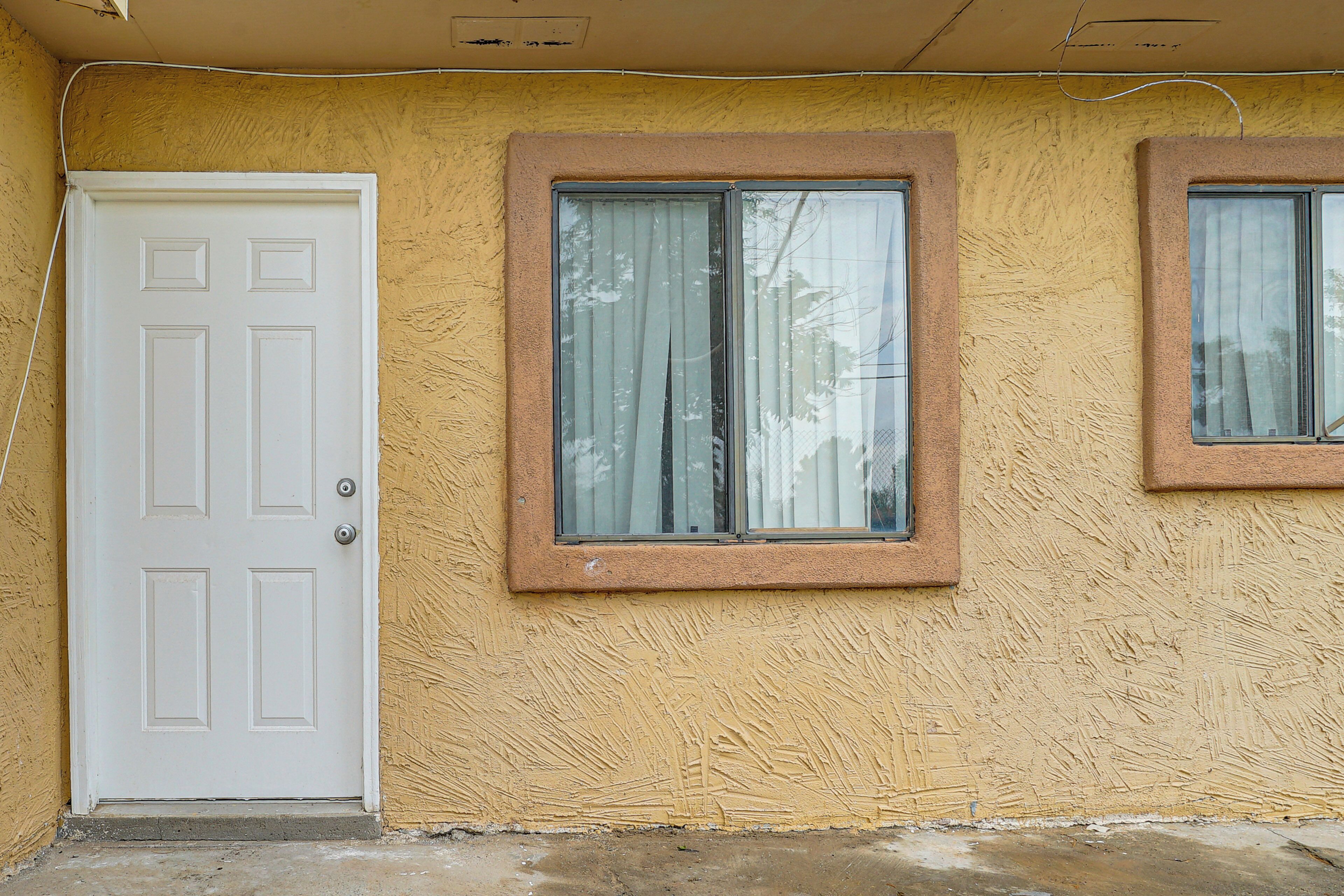 Fachada de edificio con una puerta blanca, dos ventanas con cortinas y una pared amarilla texturizada.