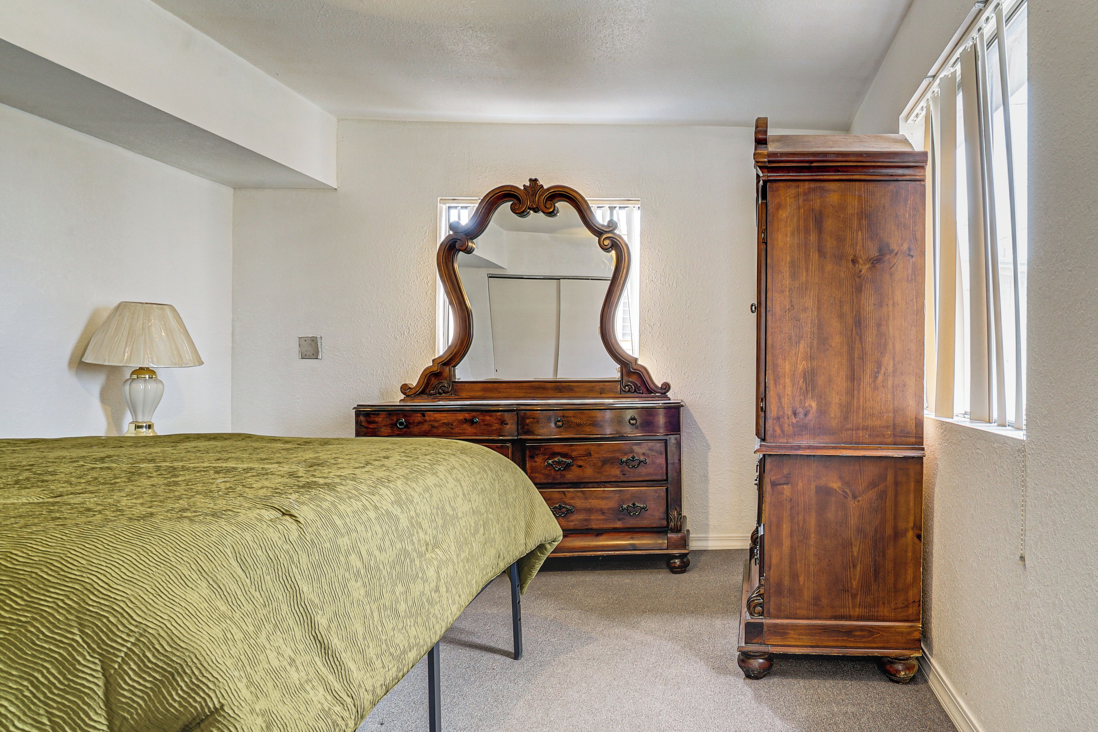 A bedroom with a bed, a dresser, a mirror, and a lamp.