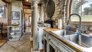 Una cucina rustica con parete in pietra, travi in legno, un'ampia finestra e un lavello.