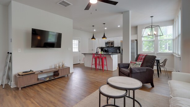 A modern living room with a flat-screen TV, a ceiling fan, a dining area with red chairs, and a kitchen in the background. - Near Centennial Park! Fayetteville Extended Stay (Fayetteville)