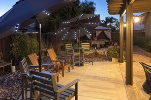 Un patio al aire libre con sillas de madera y sombrillas, piso de concreto y valla de madera.