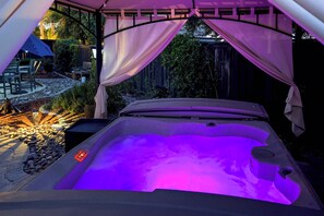 Un jacuzzi con luz púrpura, rodeado por un porche cubierto con sillas y una mesa.