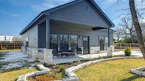 Una casa moderna de dos pisos con un porche cubierto, cimientos de piedra y un patio cercado.