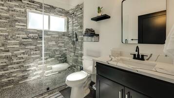 A modern bathroom with a glass shower enclosure, a white toilet, a black vanity with a mirror, and a marble countertop.