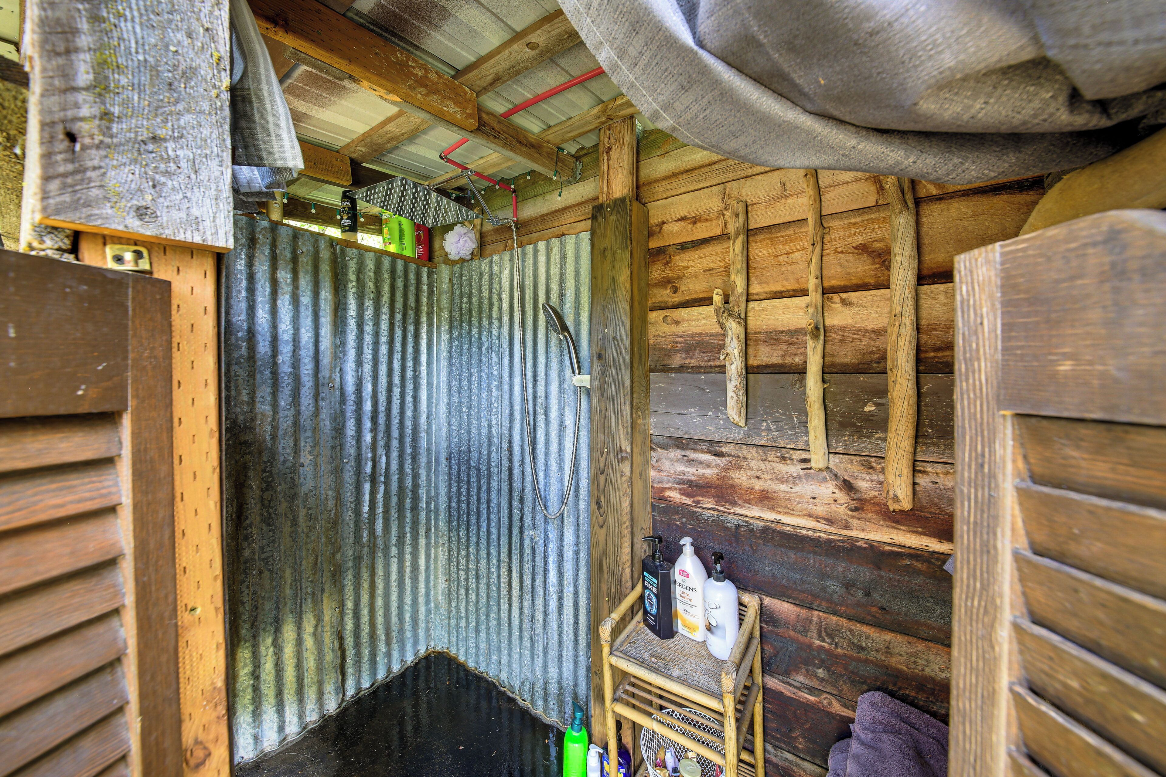A rustic cabin interior with wooden walls, a corrugated metal door, and a small wooden shelf with toiletries.