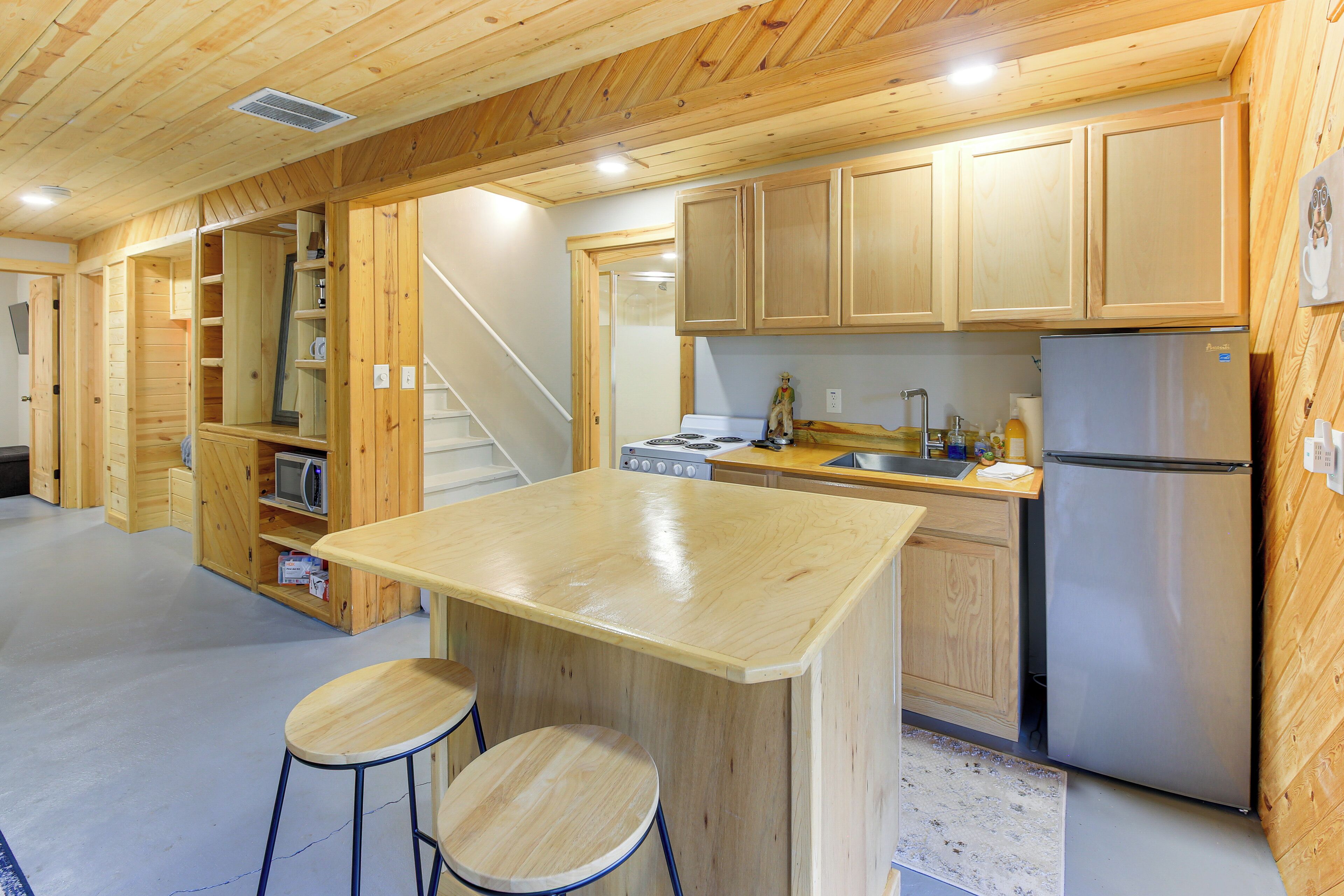 A wooden interior with a kitchen area, including a refrigerator, stove, and bar stools.