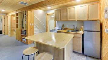 A wooden interior with a kitchen area, including a refrigerator, stove, and bar stools.