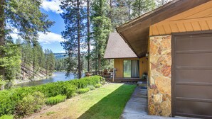 A cabin with a stone exterior, a deck, and a view of a river and forest. - Kettle River Retreat w/ Grill + Outdoor Shower (Kettle Falls)