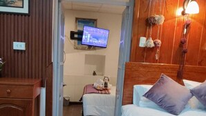Ett hotellrum med en väggpanel av trä, en tv, en säng med ett vitt och lila överkast, ett litet bord med en vas och ett träskåp.
