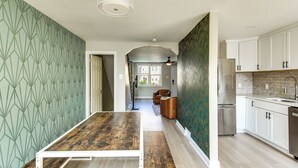 Une cuisine moderne avec des meubles blancs, une table à manger en bois et un mur orné d’un motif.