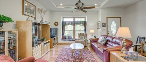 A living room with a sofa, armchair, coffee table, bookshelf, television, and a ceiling fan.