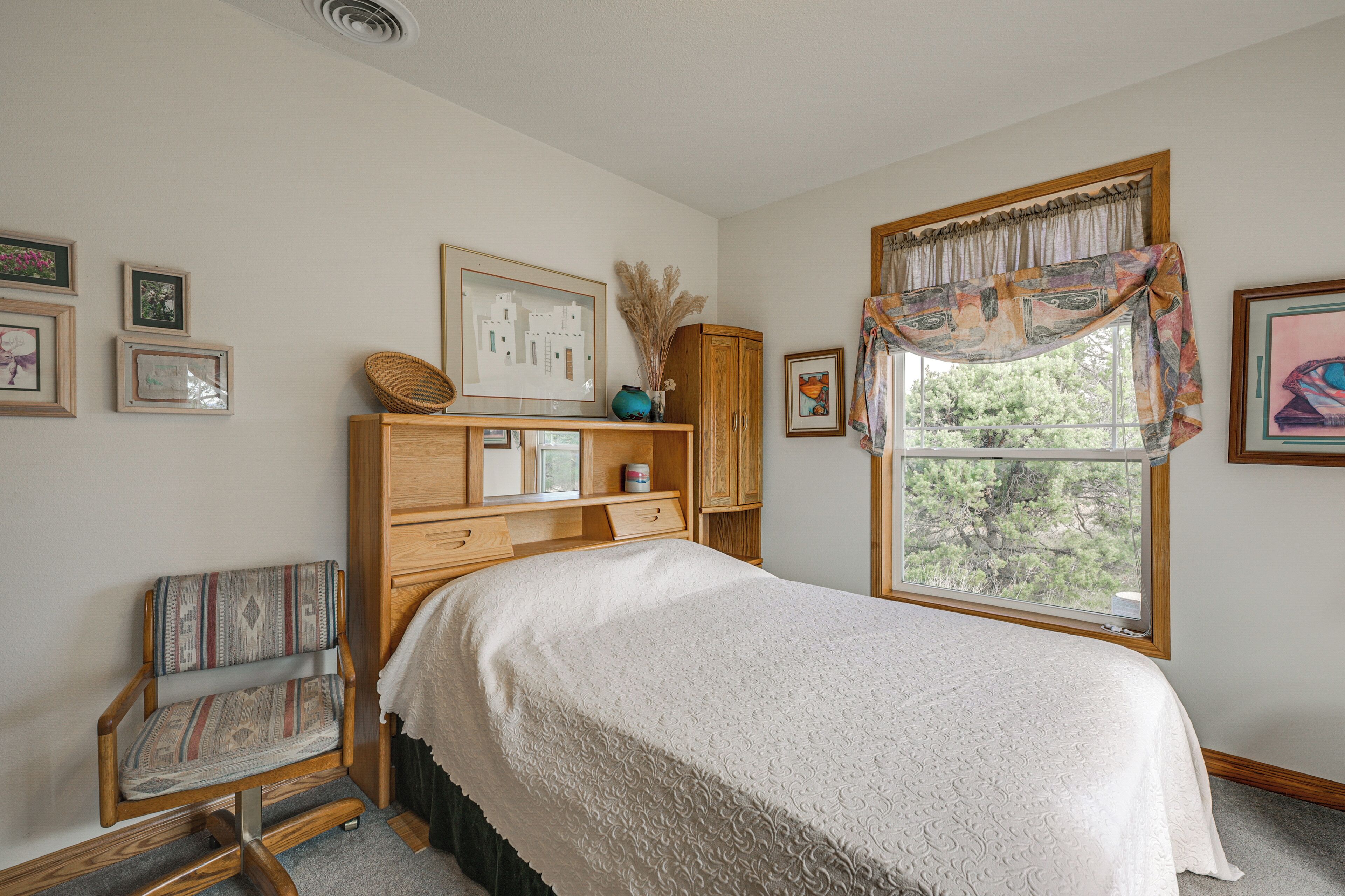 A bedroom with a bed, a chair, a wooden cabinet, and a window with a view.