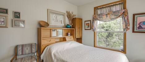 A bedroom with a bed, a chair, a wooden cabinet, and a window with a view.