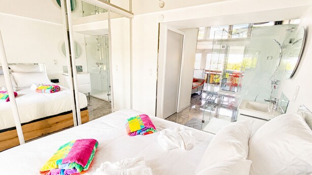 Ein modernes Hotelzimmer mit einem großen Bett, einer Glasdusche und einem Balkon mit Sitzgelegenheit.